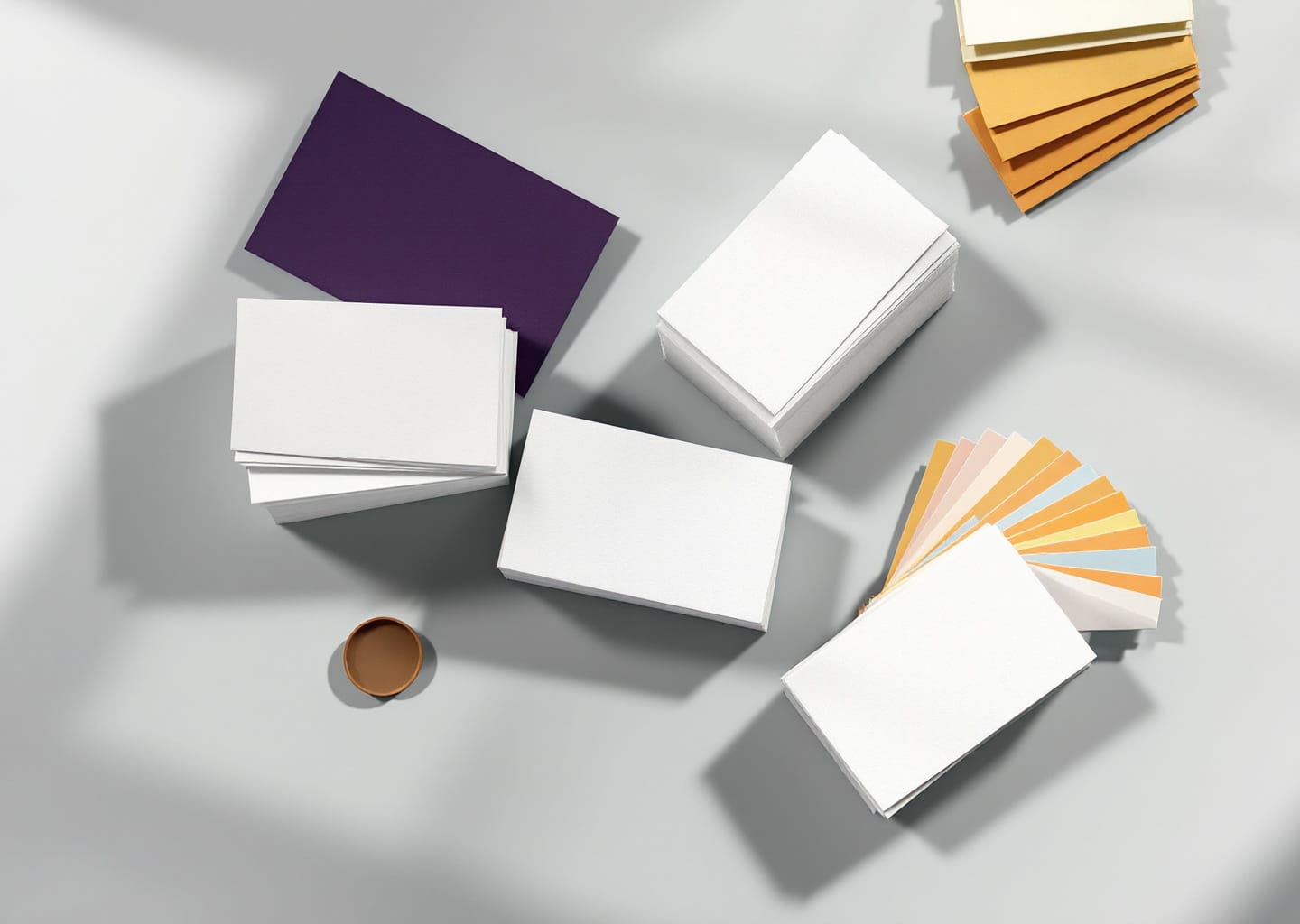 Pilas de tarjetas de presentación en blanco, una tarjeta morada y abanicos de muestras de papel de colores sobre una mesa gris